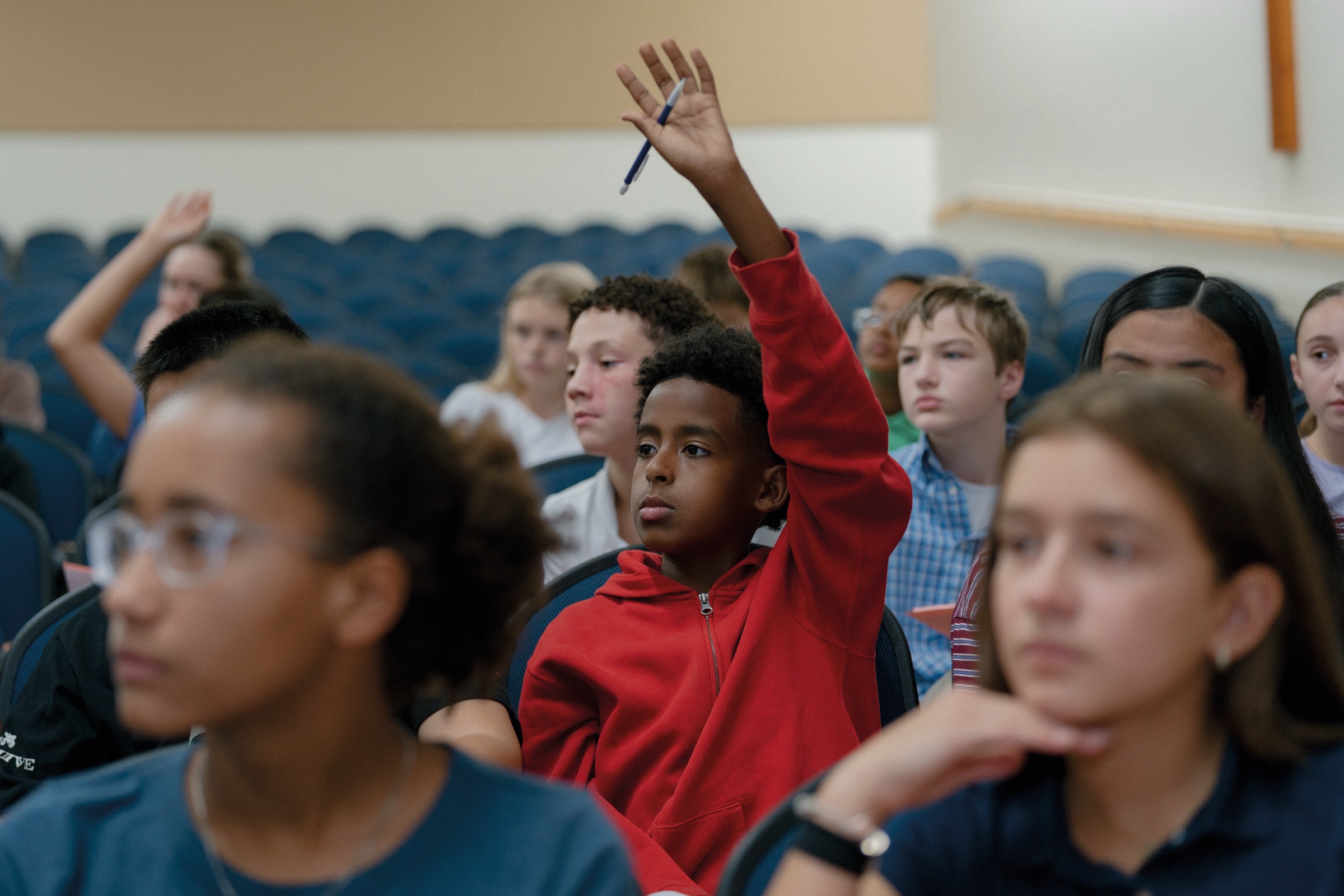 A middle school student raising a hand in a full classroom